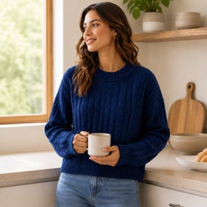 May include: A dark blue cable knit sweater with a crew neckline and long sleeves, paired with light blue denim jeans. The sweater features a vertical textured pattern and ribbed cuffs, hem, and collar, providing a classic look for casual wear.