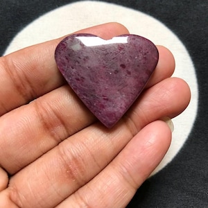 Könnte beinhalten: Ein polierter herzförmiger Stein mit einer tief magentafarbenen und dunkelvioletten, gesprenkelten Oberfläche. Der Stein hat ein glattes, glänzendes Finish mit sichtbaren natürlichen Mineraleinschlüssen und einer ausgeprägten Spitze.
