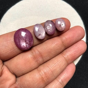 May include: Four oval-shaped cabochon gemstones in varying sizes. The largest stone is a deep magenta-pink, while the three smaller stones are a lighter, translucent pale pink with visible internal inclusions and smooth, polished surfaces.