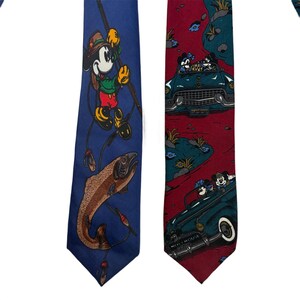 Può includere: Due cravatte con personaggi Disney. La cravatta blu mostra Topolino che pesca una grande trota. La cravatta bordeaux presenta un motivo ripetuto di Topolino e Minni che viaggiano su un'auto decappottabile vintage color verde acqua.