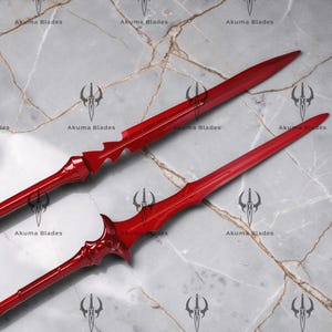 May include: Two glossy red blades with sharp, pointed tips and intricate hilt designs. The top blade features a serrated edge near the base, while the bottom blade has a curved, ornate guard. Both blades are marked with the text Akuma Blades.