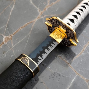 May include: A katana sword featuring a black blade with a distinct wavy hamon line, a gold-colored tsuba with intricate black engravings, and a white-wrapped handle. The scabbard is black with a textured finish and gold-colored metal accents.