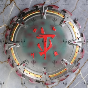 Puede incluir: Un escudo circular con acabado plateado metálico, que presenta un símbolo rojo prominente en el centro. El borde exterior está acentuado con adornos dorados y múltiples protuberancias plateadas en forma de garra con puntas rojas.