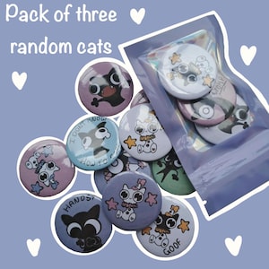 May include: A collection of round pin-back buttons featuring various cartoon cat illustrations in colours including purple, blue, and green. Some buttons are loose, while others are contained within a clear plastic pouch. Text includes "I DONT KNOW HOW TO COOL", "HANDS", and "GOOF".