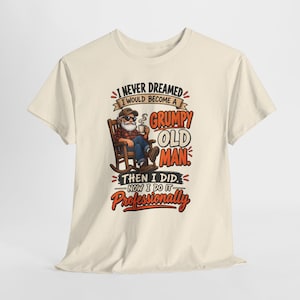 以下が含まれることがあります： クリーム色の半袖Tシャツ。サングラスをかけ、マグカップを持ってロッキングチェアに座る髭を生やした人物のグラフィックが描かれています。テキストは「I NEVER DREAMED I WOULD BECOME A GRUMPY OLD MAN THEN I DID. NOW I DO IT Professionally.」と書かれています。