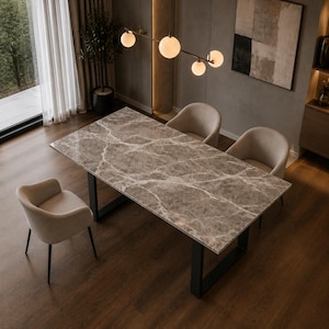 Peut inclure: Une table à manger rectangulaire avec un plateau en marbre gris poli aux veines blanches, soutenue par deux pieds en métal noir en forme de U. Trois fauteuils beiges rembourrés avec des pieds noirs sont disposés autour de la table.