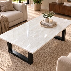 May include: A rectangular coffee table featuring a white, tiled surface with a glossy finish and a distinct brick-like pattern. The table is supported by two sturdy, black metal U-shaped legs that provide a stable base for the tabletop.