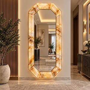 May include: A tall, octagonal wall mirror featuring a backlit frame with a polished amber and gold marble pattern. The reflective glass surface is surrounded by a glowing, translucent stone-like border that illuminates the surrounding wall area.
