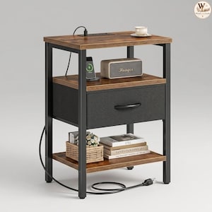 May include: A bedside table with a black metal frame and two brown wood-grain shelves. It features a central fabric drawer with a black handle, a top surface with a built-in power outlet, and a bottom shelf holding a woven basket and books.