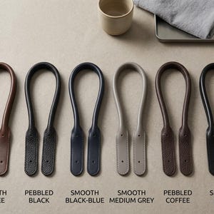 Puede incluir: Seis asas de bolso en forma de U dispuestas en fila, con varias texturas y colores: caf&eacute; liso, negro granulado, azul-negro liso, gris medio liso, caf&eacute; granulado y negro liso. Cada asa tiene dos extremos planos con orificios perforados.