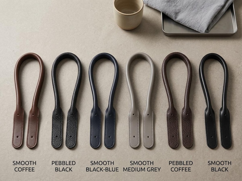 Puede incluir: Seis asas de bolso en forma de U dispuestas en fila, con varias texturas y colores: caf&eacute; liso, negro granulado, azul-negro liso, gris medio liso, caf&eacute; granulado y negro liso. Cada asa tiene dos extremos planos con orificios perforados.