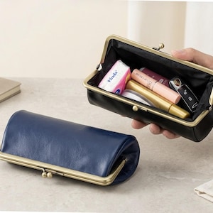 May include: Two rectangular pouches with brass-toned metal kiss-lock frames. One pouch is navy blue and closed, while the other is black and open, containing small personal items including a pink tissue pack, lip balm, and a black car key fob.