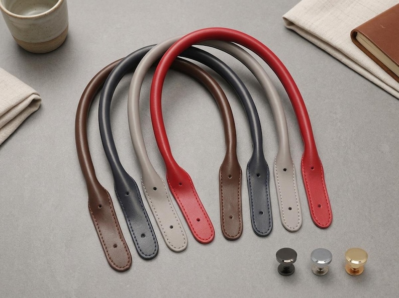 Puede incluir: Cuatro asas de bolso arqueadas en marr&oacute;n, gris oscuro, gris claro y rojo, cada una con extremos cosidos con dos orificios preperforados para su fijaci&oacute;n. Tres peque&ntilde;os cierres met&aacute;licos redondos en negro, plata y oro se sit&uacute;an debajo.