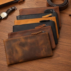 May include: A collection of rectangular leather zipper pouches arranged in a stack. The pouches feature various shades of brown and black leather with visible grain textures and metal zipper closures with leather pull tabs attached to each one.