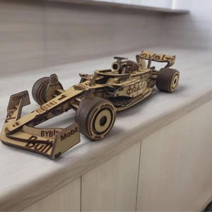 Pode incluir: Um modelo de madeira cortado a laser de um carro de corrida de Fórmula 1 com a pintura da Oracle Red Bull Racing. O carro inclui textos de patrocinadores visíveis como Oracle, Mobil, Bybit e Claro, com cockpit detalhado e quatro rodas.
