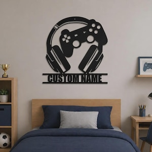 May include: A black metal wall sign featuring a gaming headset and a game controller silhouette positioned above a horizontal bar with the text CUSTOM NAME in a bold, sans-serif font, designed for wall mounting in a bedroom or gaming space.