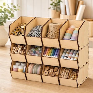 May include: A light-colored wooden storage organizer featuring twelve open-front bins arranged in three rows and four columns. The bins are filled with various craft supplies including metal clips, beads, twine, spools of ribbon, and buttons.