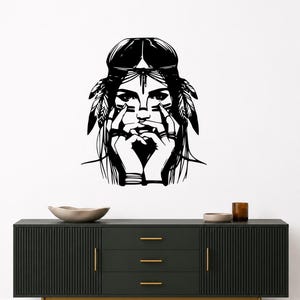 May include: A black wall decal featuring a stylized illustration of a person with long hair, wearing a headband with feathers on both sides. The person has their hands positioned near their face, with fingers touching the cheeks and chin area.