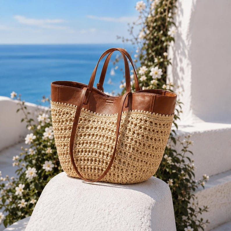 May include: A tote bag featuring a tan woven straw body with a wide, smooth brown leather upper section and two matching brown leather shoulder straps. The transition between the straw and leather is finished with a decorative scalloped edge.