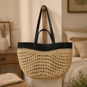May include: A tote bag featuring a natural beige woven straw body with an open-knit pattern and a smooth black leather top panel. The bag includes two black leather shoulder straps with visible white stitching, creating a contrast between the textures.