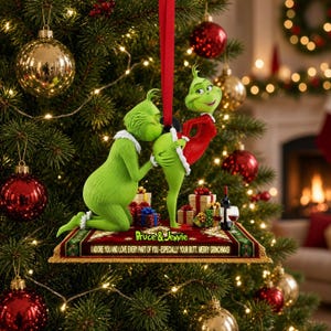 Könnte beinhalten: Ein hängender Weihnachtsbaumschmuck mit zwei grünen Grinch-ähnlichen Figuren auf einem rechteckigen Sockel mit rotem Band. Der Sockel zeigt den Text 'Bruce & Jennie' und 'I ADORE YOU AND LOVE EVERY PART OF YOU - ESPECIALLY YOUR BUTT. MERRY GRINCHMAS!'