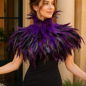 May include: A high-neck feather collar featuring layered, deep purple and iridescent black feathers. The collar sits around the neck and covers the shoulders, worn over a simple black sleeveless dress. The feathers are dense and textured.
