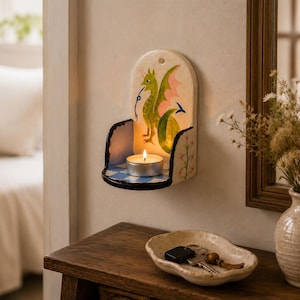 May include: A wall-mounted ceramic candle holder featuring a hand-painted green dragon on the back panel, a blue and white checkered base, and a lit tea light candle. The side panels are decorated with floral motifs and dark painted edges.