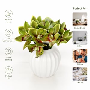 Puede incluir: Un ramo de orquídeas cymbidium artificiales de color verde con centros rojo oscuro, dispuesto en un jarrón de cerámica blanco, redondo y acanalado. Las flores presentan pétalos superpuestos con degradados realistas y composición limpia.