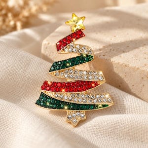 May include: A gold-tone metal brooch shaped like a Christmas tree, featuring a spiraling design adorned with alternating rows of red, green, and clear sparkling rhinestones, topped with a single yellow star-shaped crystal at the apex.