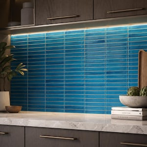 May include: A kitchen backsplash featuring rectangular, glossy blue ceramic tiles arranged in a horizontal stacked pattern. The tiles have a vibrant, deep blue hue with subtle variations in tone and are illuminated by under-cabinet lighting.