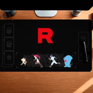 Puede incluir: Un tapete de juego rectangular negro con una letra R roja grande en el centro. La sección inferior muestra personajes de dibujos animados coloridos, incluyendo una criatura felina, una persona con cabello largo rosa, una persona con cabello azul y una figura azul.