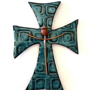 Op de afbeelding: Een turquoise kruis met een getextureerd oppervlak en koperen details. Het kruis heeft een centrale bruine bol en koperen lijnen. Het ontwerp heeft een rustieke, handgemaakte uitstraling, geschikt voor wanddecoratie.