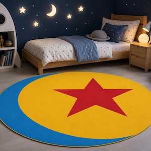 May include: A circular area rug featuring a large yellow field with a prominent red five-pointed star in the center and a thick blue crescent shape along the left edge, designed with a bold graphic pattern inspired by space and celestial themes.