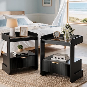May include: Two black nightstands with a C-shaped frame, a top surface, and a lower drawer featuring a vertical ribbed front and a gold handle. The left nightstand holds a marble-base lamp and a picture frame, while the right holds a clock and flowers.