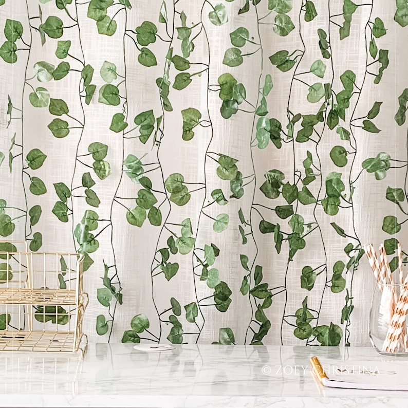 May include: White sheer curtains with a green leaf pattern. The curtains are hung on a window and there is a white countertop in front of them.