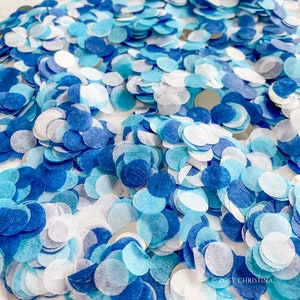 May include: A close-up image of blue and white confetti. The confetti is made of paper and is scattered on a white surface.