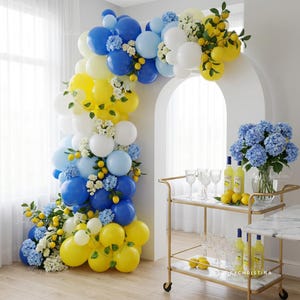 May include: A festive balloon arch in shades of blue, yellow, and white, adorned with faux lemons and white flowers. A gold bar cart with glasses, bottles, and lemons complements the decor, creating a cheerful party atmosphere.