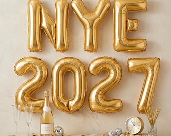 May include: Gold foil balloons spelling NYE 2027 arranged in two rows. Below the balloons sits a bottle of champagne, two empty stemmed glasses, a round analog clock, and a small silver decorative sphere on a table with scattered gold confetti.