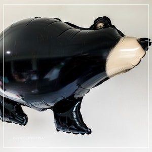 May include: Black and white balloon shaped like a bear. The bear has a white nose and a black body.
