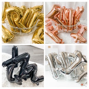 Op de afbeelding: Vier sets letterballonnen in verschillende kleuren: goud, ros&eacute; goud, zwart en zilver. Elke set is gerangschikt in een draadmand.