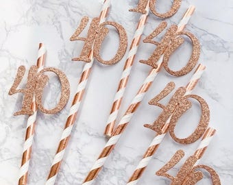 Könnte beinhalten: Partydekorationen zum 40. Geburtstag. Strohhalme mit weißen und kupferfarbenen Streifen, gekrönt von roségoldenen Glitzer-Zahlen "40".