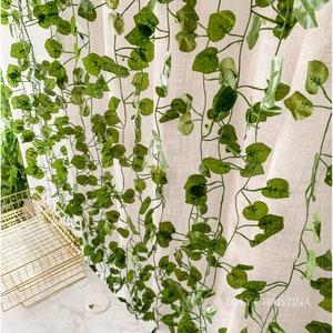 May include: A white sheer curtain with a green artificial vine garland draped over it. The garland features realistic-looking leaves and stems.