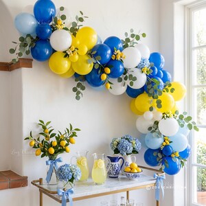 May include: A festive party scene with a balloon arch in blue, white, and yellow, adorned with greenery and lemons. A bar cart displays lemonade, blue hydrangeas, and lemons. The scene is bright and cheerful, perfect for a summer celebration.