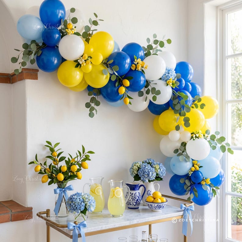 May include: A festive party scene with a balloon arch in blue, white, and yellow, adorned with greenery and lemons. A bar cart displays lemonade, blue hydrangeas, and lemons. The scene is bright and cheerful, perfect for a summer celebration.
