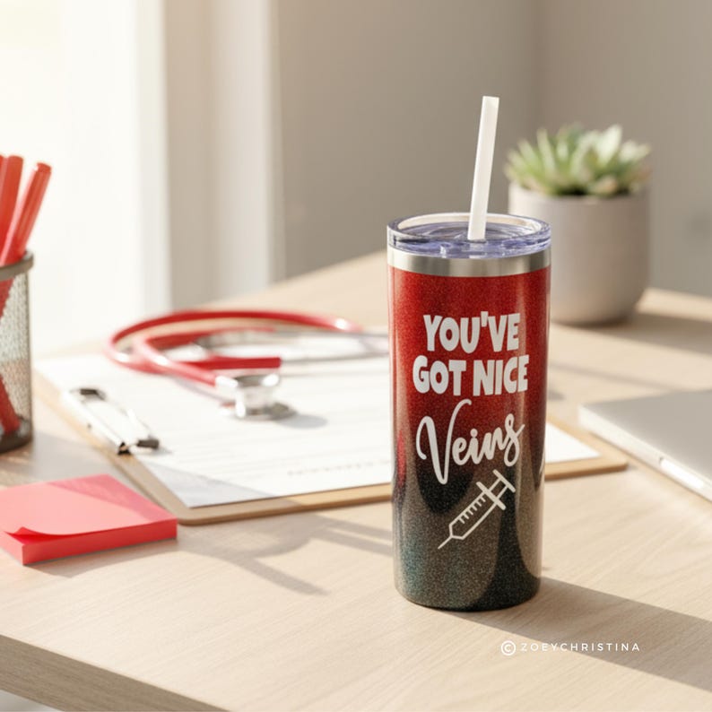 May include: A red and black glitter tumbler with a white straw. The tumbler has the text "YOU'VE GOT NICE Veins" and a syringe graphic. A stethoscope, notepad, and pen holder are in the background.