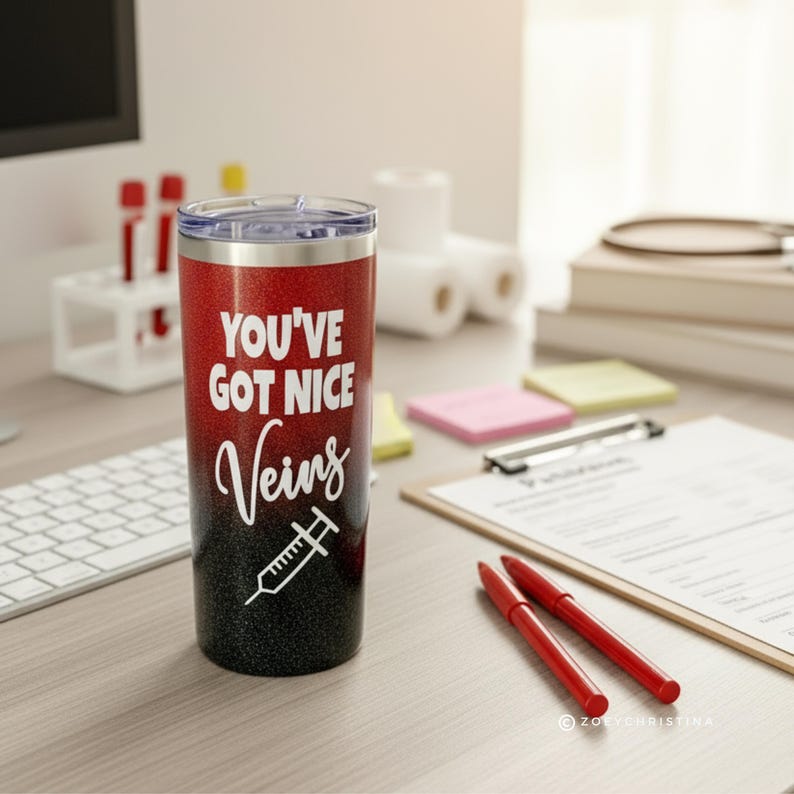 May include: A red and black glitter tumbler with the text "YOU'VE GOT NICE Veins" and a syringe graphic. The tumbler has a silver rim and a clear lid. The design is white. The tumbler is on a desk with medical supplies.