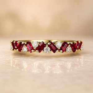 May include: A yellow gold band ring featuring an alternating pattern of baguette-cut red rubies and round brilliant-cut white diamonds set in a continuous row across the top of the metal band, creating a vibrant and symmetrical gemstone design.