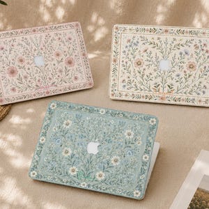Peut inclure: Trois étuis pour ordinateur portable rectangulaires avec des motifs floraux complexes. Un étui est rose avec des fleurs délicates, un est crème avec des fleurs bleues et roses, et un est vert sauge avec des motifs floraux blancs et bleus.