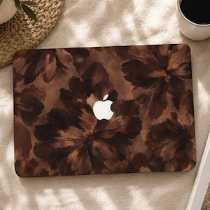 Op de afbeelding: Een rechthoekige laptophoes met een donkerbruin en zwart bloemenpatroon in aquarel-stijl en een centrale uitsparing die het witte Apple-logo onthult. De hoes heeft afgeronde hoeken en een gladde afwerking met grote, abstracte bloemblaadjes.