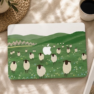 Puede incluir: Una funda para portátil con un paisaje pintado de colinas verdes y un rebaño de ovejas con cara negra y lana blanca. El diseño incluye una hilera de árboles con flores rosas al fondo y pequeñas flores silvestres esparcidas por la hierba.